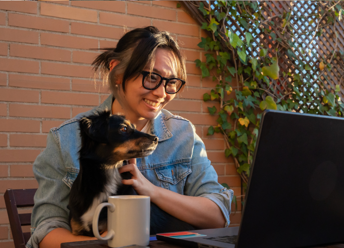 Person lovingly holding holding their dog while drinking coffee and looking a laptop computer on a patio
